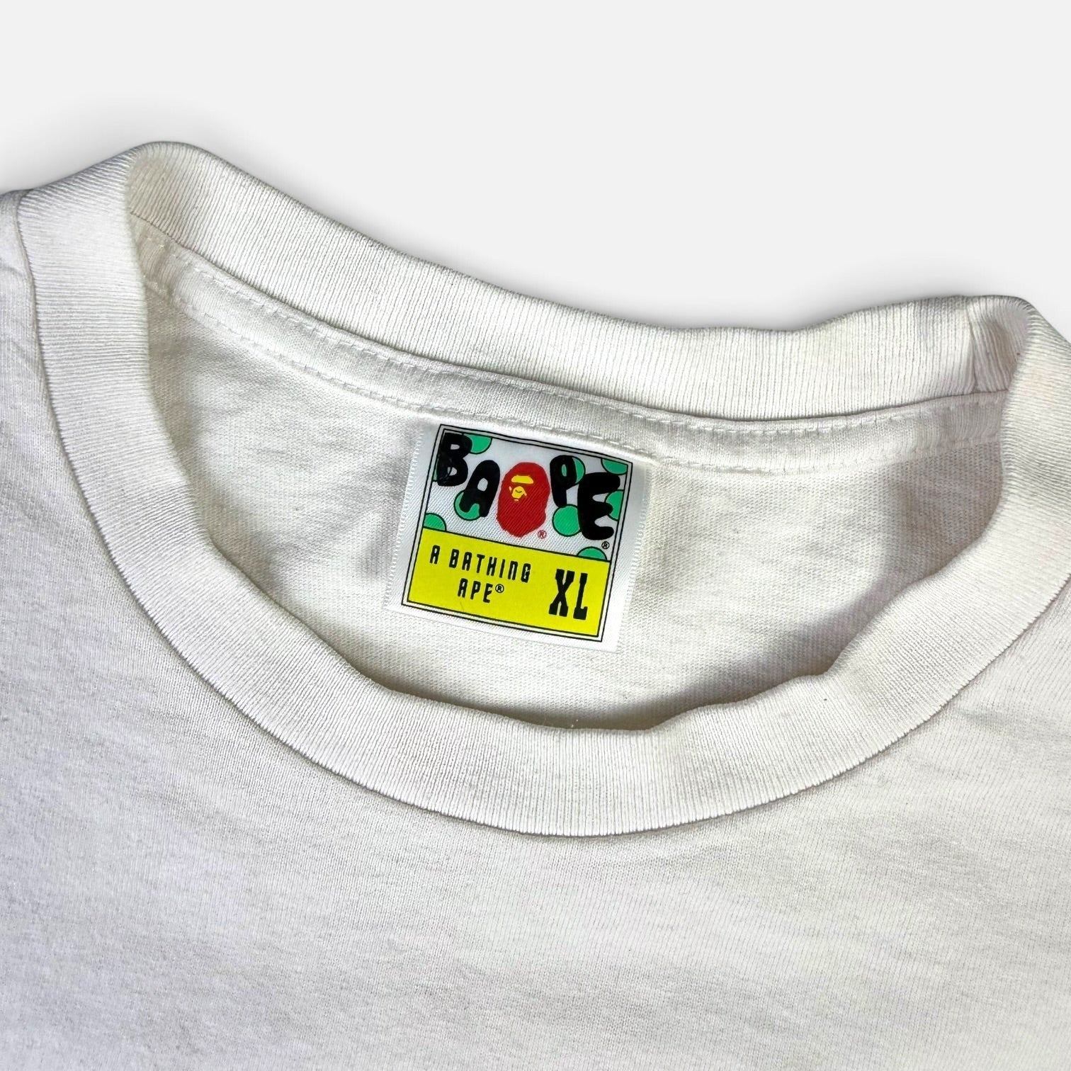 V STEALS white BAPE t-shirt featuring a vintage A Bathing Ape neck label with size XL on a yellow background
